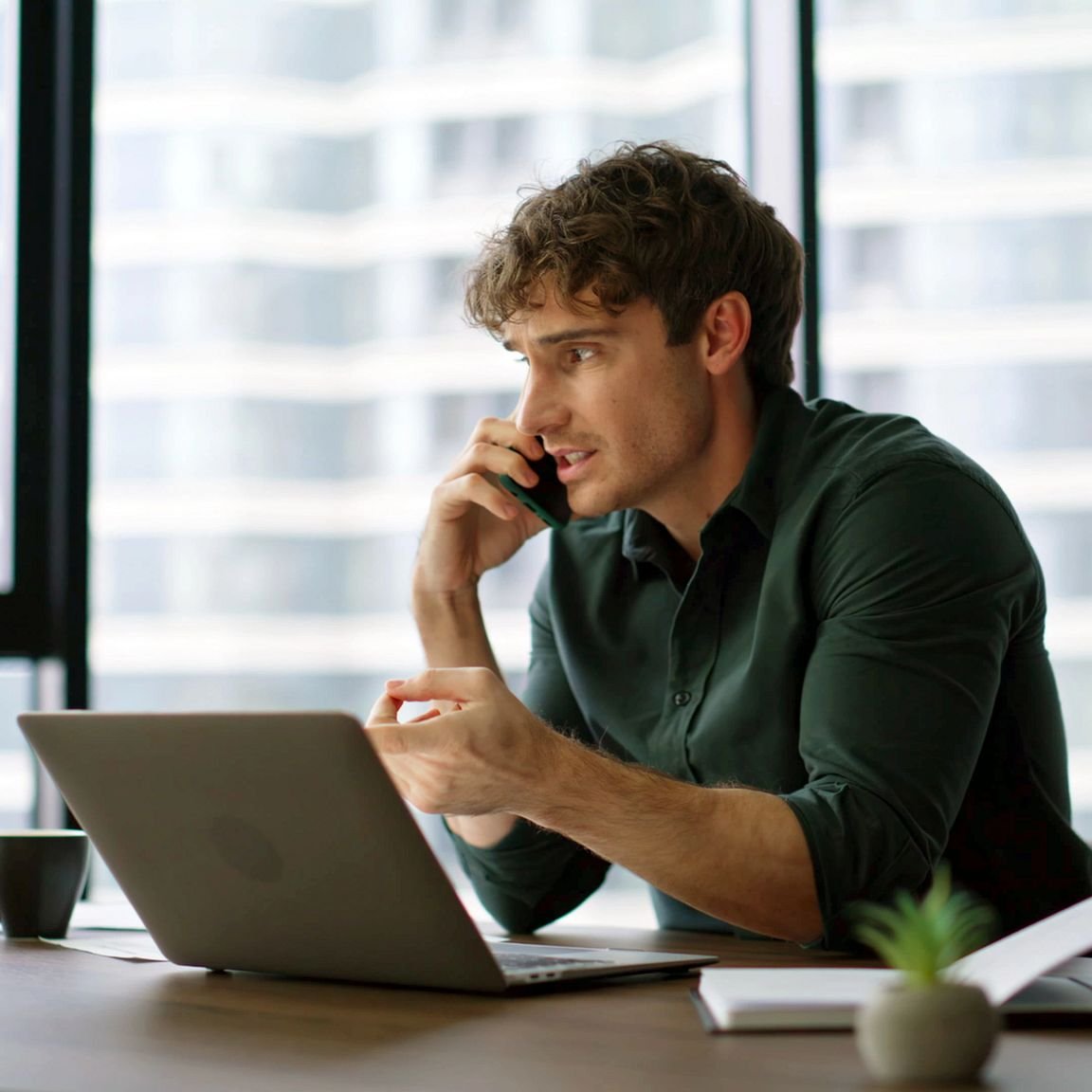 junger Mann telefoniert mit Handy am Laptop