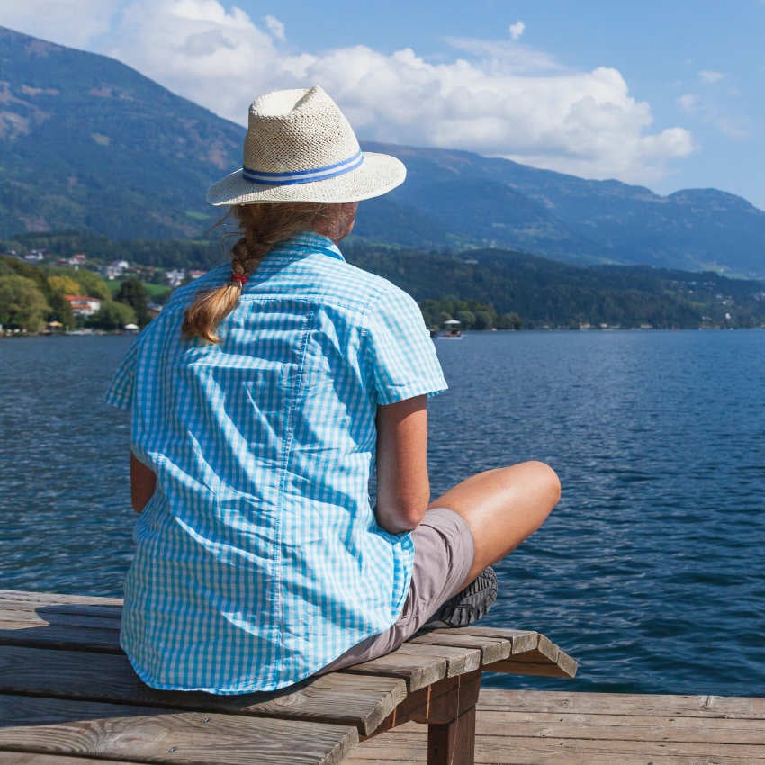 W4GK6R_850x850 Frau sitzt auf Steg und blickt über einen See