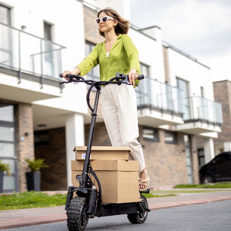 Junge Frau mit Sonnenbrille transportiert Pakete auf E-Scooter
