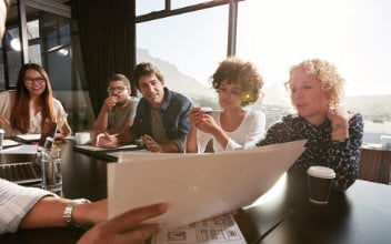 eigentuemergemeinschaft_352x220_2023_11 Nahaufnahme der Hände eines jungen Mannes, der anderen Menschen ein Dokument erläutert