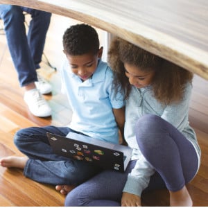 Kinder spielen unter einem Tisch an Laptop