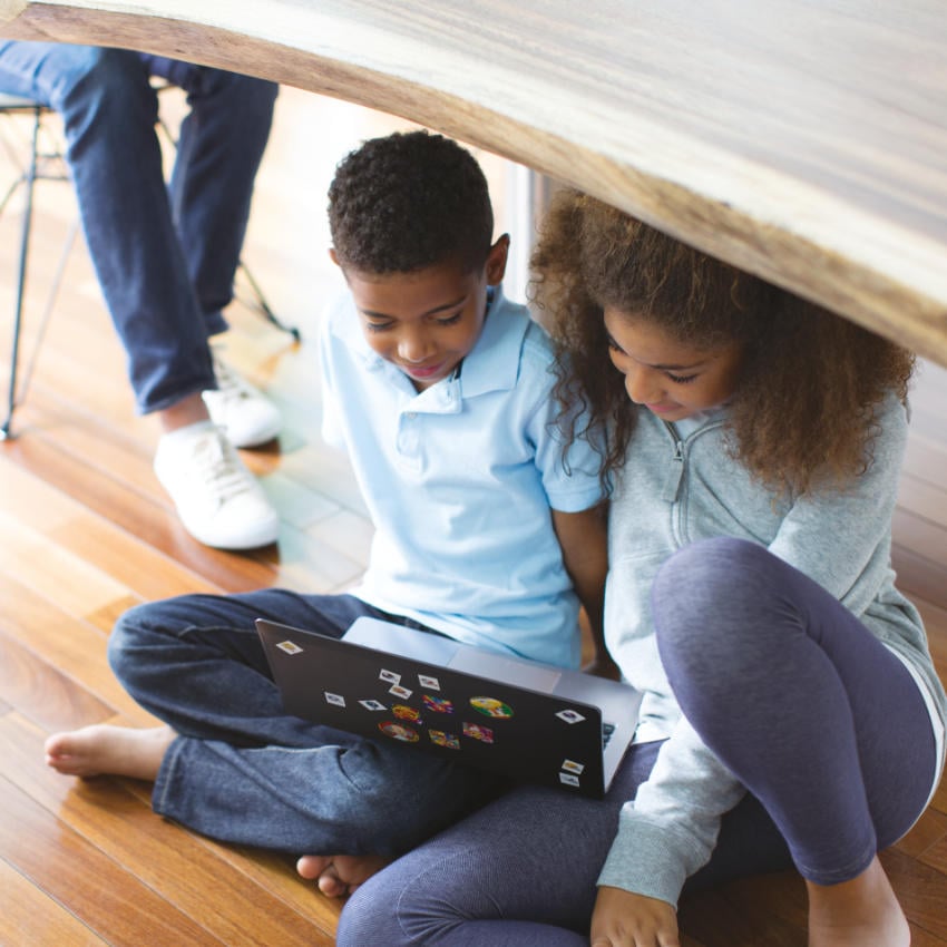 Kinder spielen unter einem Tisch an Laptop