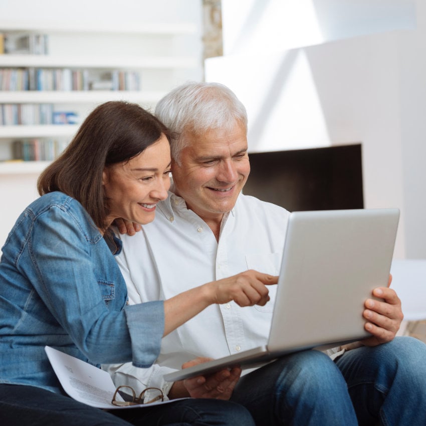 Paar sitzt zusammen auf einem Sofa und schaut gemeinsam auf Laptop Paar sitzt zusammen auf einem Sofa und schaut gemeinsam auf Laptop