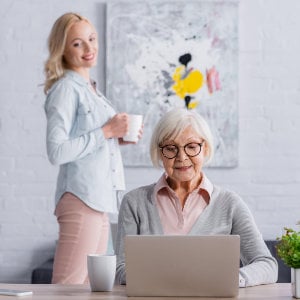 Junge Frau lächelt ältere Frau an, die an einem Laptop arbeitet
