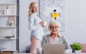 Junge Frau lächelt ältere Frau an, die an einem Laptop arbeitet