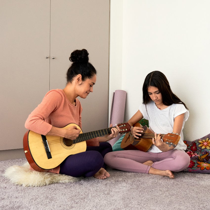 Zwei Frauen sitzen im Schneidersitz auf dem Boden und spielen Gitarre