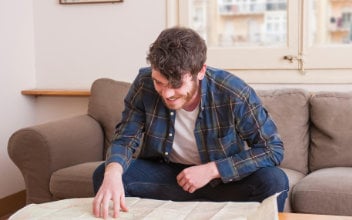 hpv-kuendigen_352x220_2023_08 junger Mann sitzt über Landkarte gebeugt auf Sofa