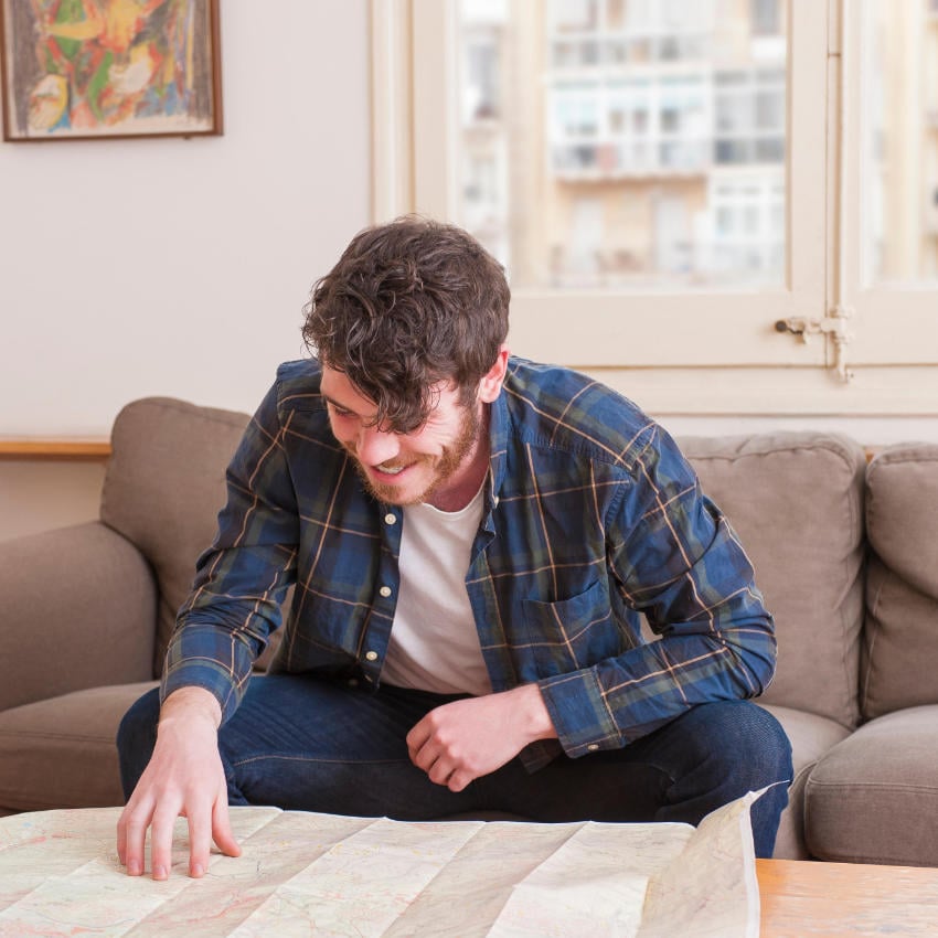 HRFPFT_850x850 junger Mann sitzt über Landkarte gebeugt auf Sofa
