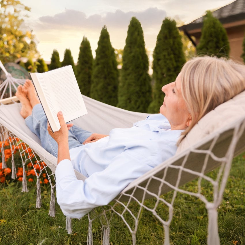 Frau liest entspannt ein Buch in der Hängematte