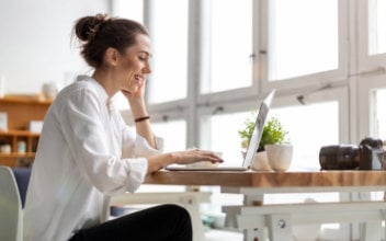 nebenkosten_352x220_2024_06 Junge Frau blickt lächelnd auf ihren Laptop