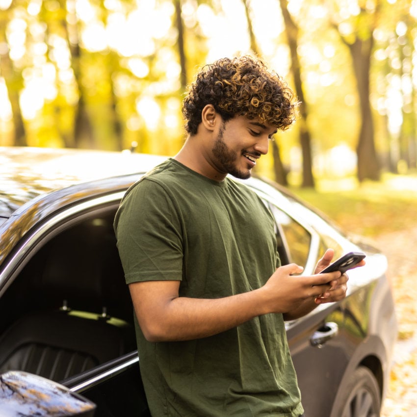 AdobeStock_545798675_850x850 Mann lehnt an seinem Auto und schaut aufs Handy