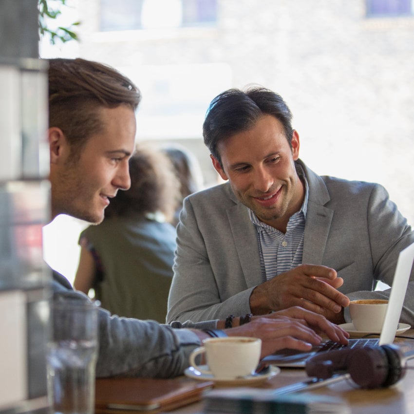 Zwei Männer arbeiten gemeinsam an einer Theke sitzend an einem Laptop