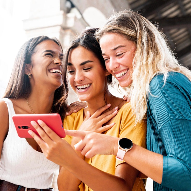 drei Freundinnen schauen zusammen lachend auf ein Handy