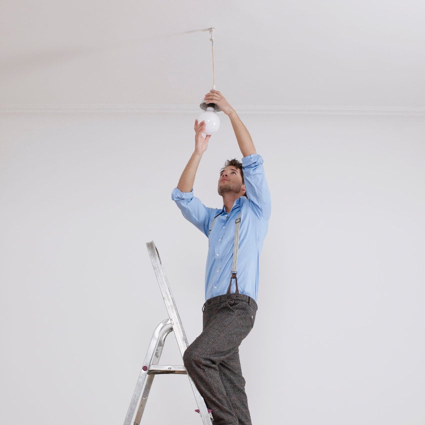 Mann auf Trittleiter schraubt Glühbirne ein