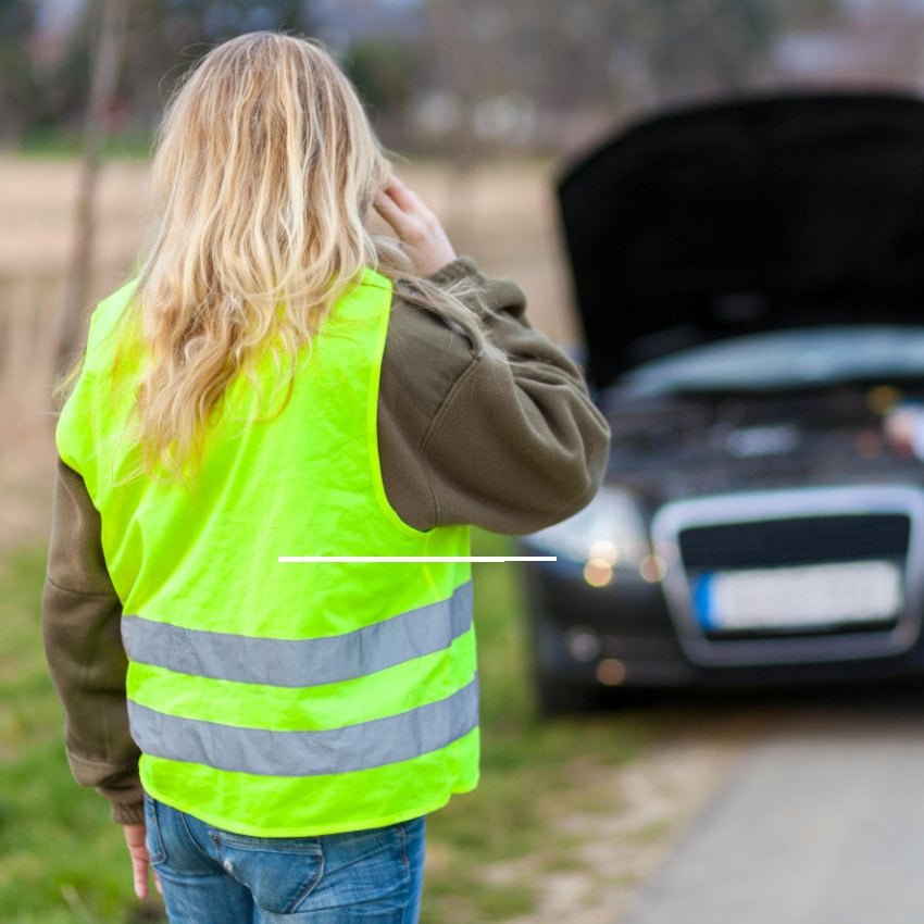 Frau mit Warnweste steht mit Auto am Straßenrand und telefoniert