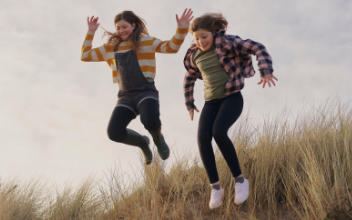 zwei Mädchen springen eine Düne runter
