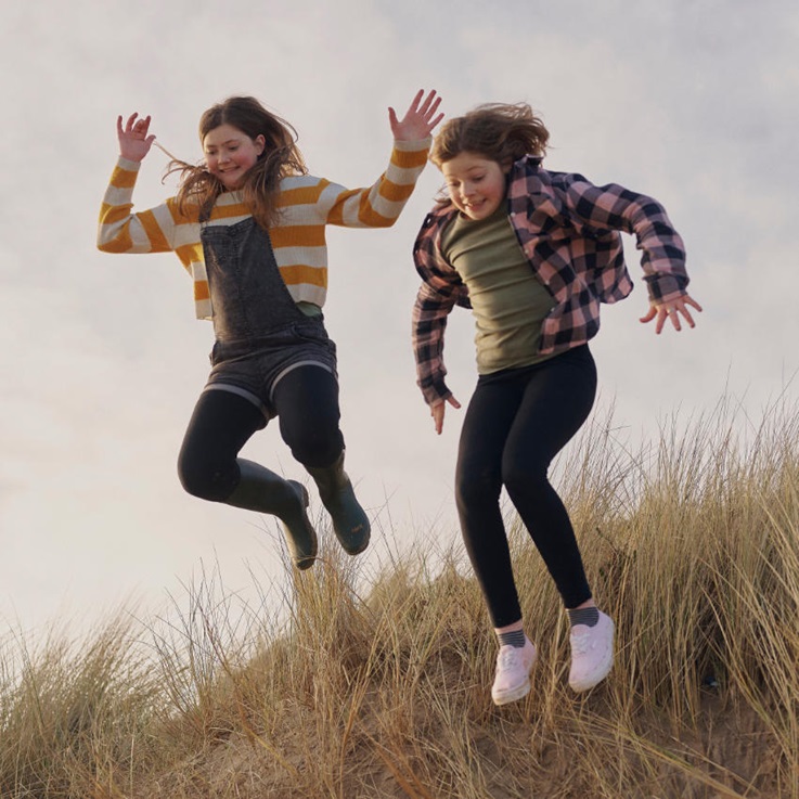 zwei Mädchen springen eine Düne runter