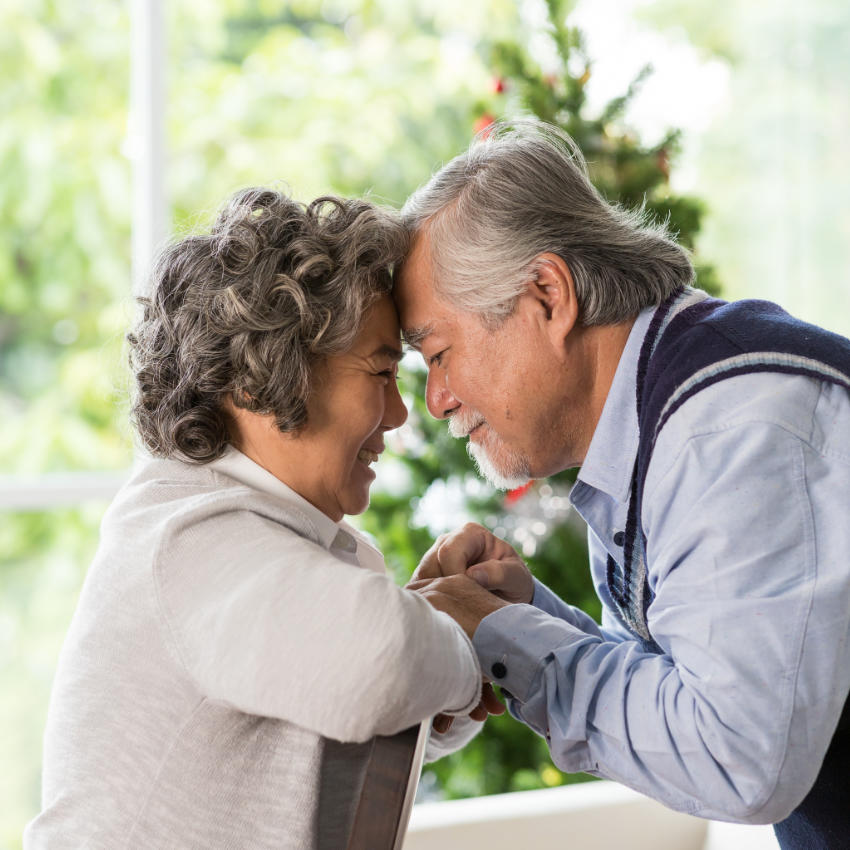 Asiatisches älteres Paar hält sich an den Händen und lehnt Stirn an Stirn