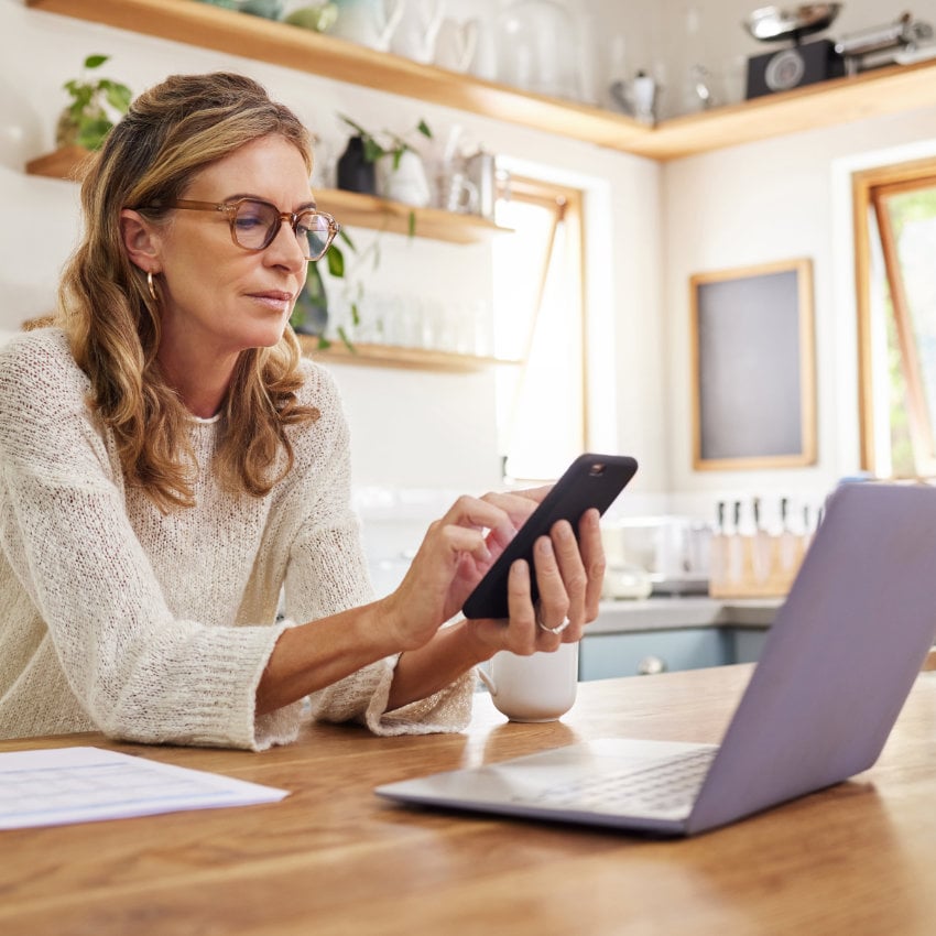 Frau sitzt vor Laptop und tippt am Handy