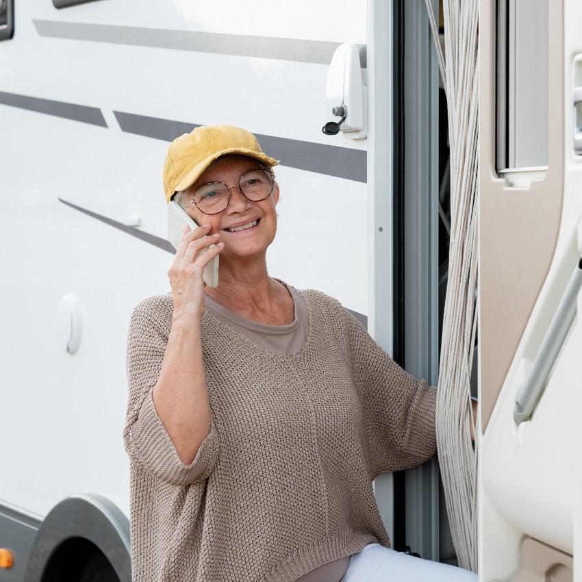 Frau telefoniert mit ihrem Handy vor Wohnmobiltür