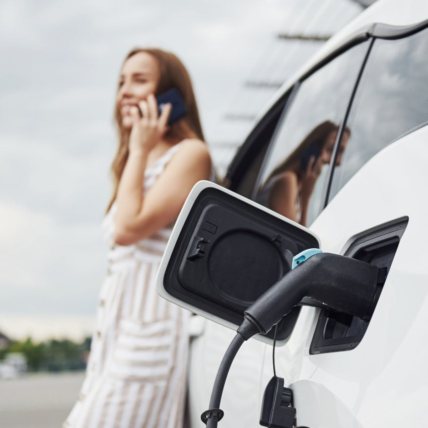 shutterstock_1479315494_850x850 Frau lehnt an ladendem E-Auto und telefoniert