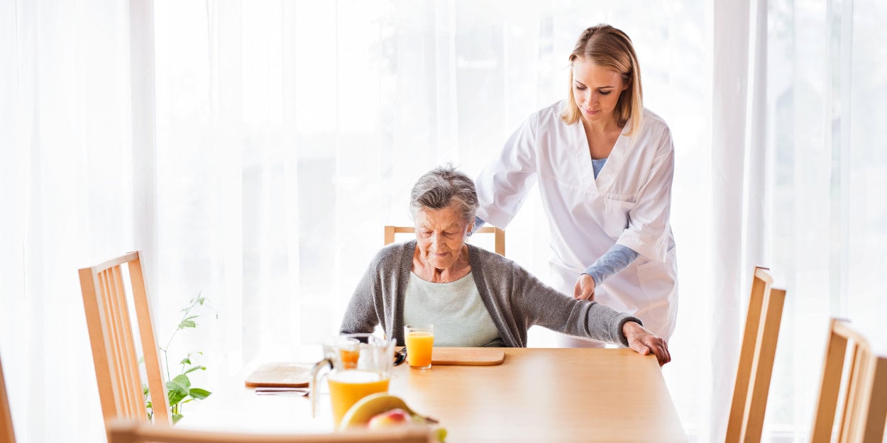 Frau rückt ältere Frau an Eßtisch