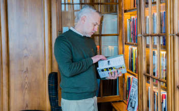 Mann vor Bücherregal blättert in einem Buch