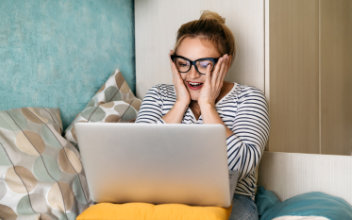 Junge Frau schaut freudig überrascht auf ihren Laptop