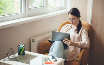 Konzentrierte junge Frau mit Brille, die im Sessel sitzend am Laptop arbeitet