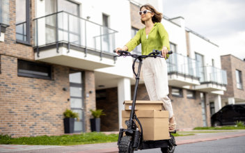 Junge Frau mit Sonnenbrille transportiert Pakete auf E-Scooter