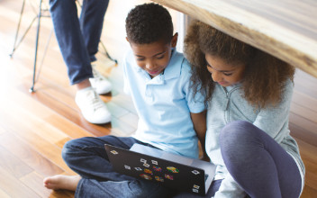 Kinder spielen unter einem Tisch an Laptop