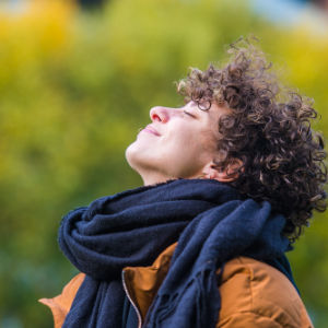 Frau mit Schal reckt ihr Gesicht der Sonne entgegen