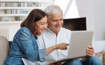 Paar sitzt zusammen auf einem Sofa und schaut gemeinsam auf Laptop
