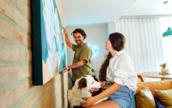 Mann hängt Bild an Wohnzimmerwand auf