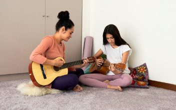 Zwei Frauen sitzen im Schneidersitz auf dem Boden und spielen Gitarre