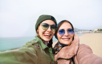 Mutter und Tochter nehmen am Strand Selfie von sich auf