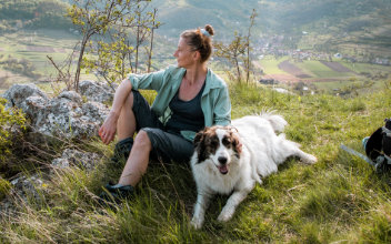 Wandererin rastet mit Hund auf einer Wiese in den Bergen