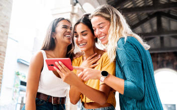 drei Freundinnen schauen zusammen lachend auf ein Handy