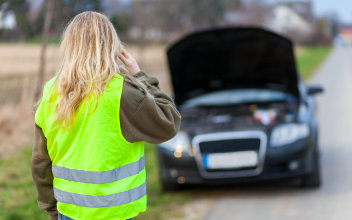 Frau mit Warnweste steht mit Auto am Straßenrand und telefoniert