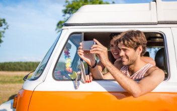 junger Mann knipst mit dem Handy aus seinem Wohnmobil