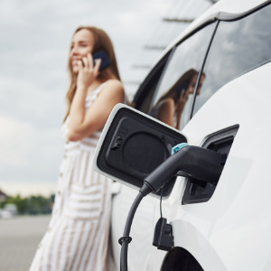 Frau lehnt an ladendem E-Auto und telefoniert