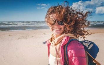 Frau mit Sonnenbrille und Rucksack am Strand