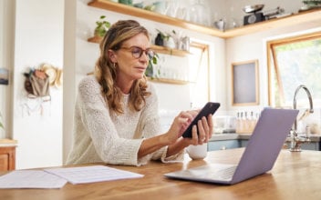 Frau sitzt vor Laptop und tippt am Handy